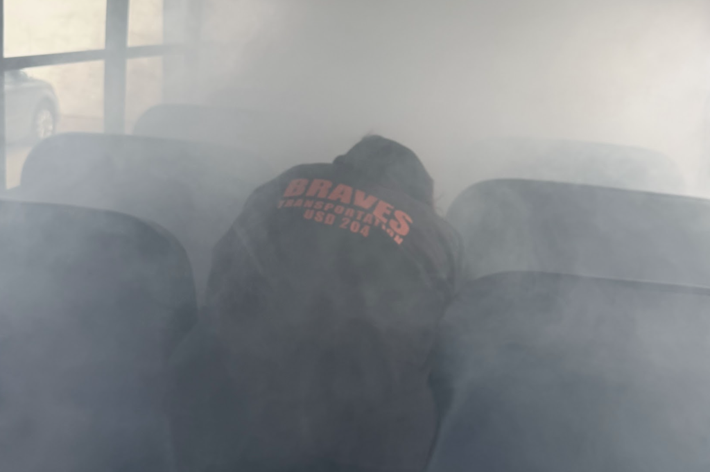 Person in a black hoodie with "Braves" on the back sitting on a chair with smoke in background.
