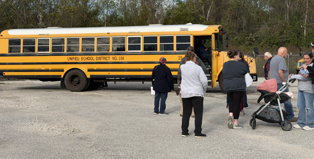 Several people stand near a parked school bus; one person enters the bus while others look on.