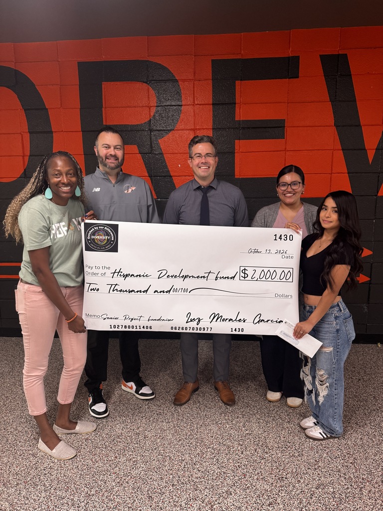 Five adults standing near an orange wall, presenting a large white check with a total amount of $20,000.