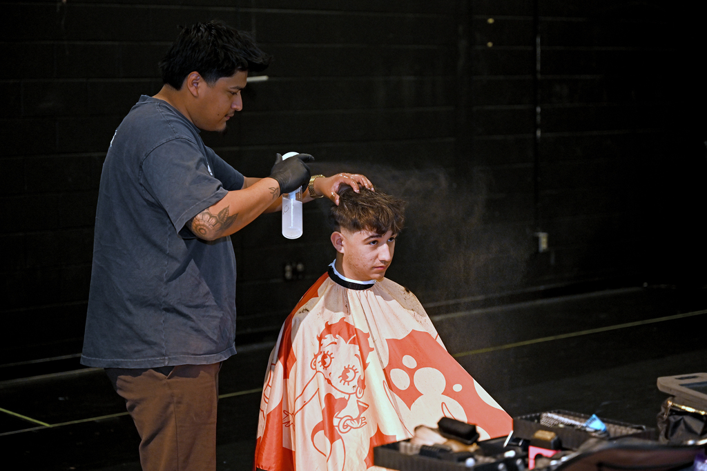 A man sprays a substance into a customer's hair while they sit in a barber's chair.
