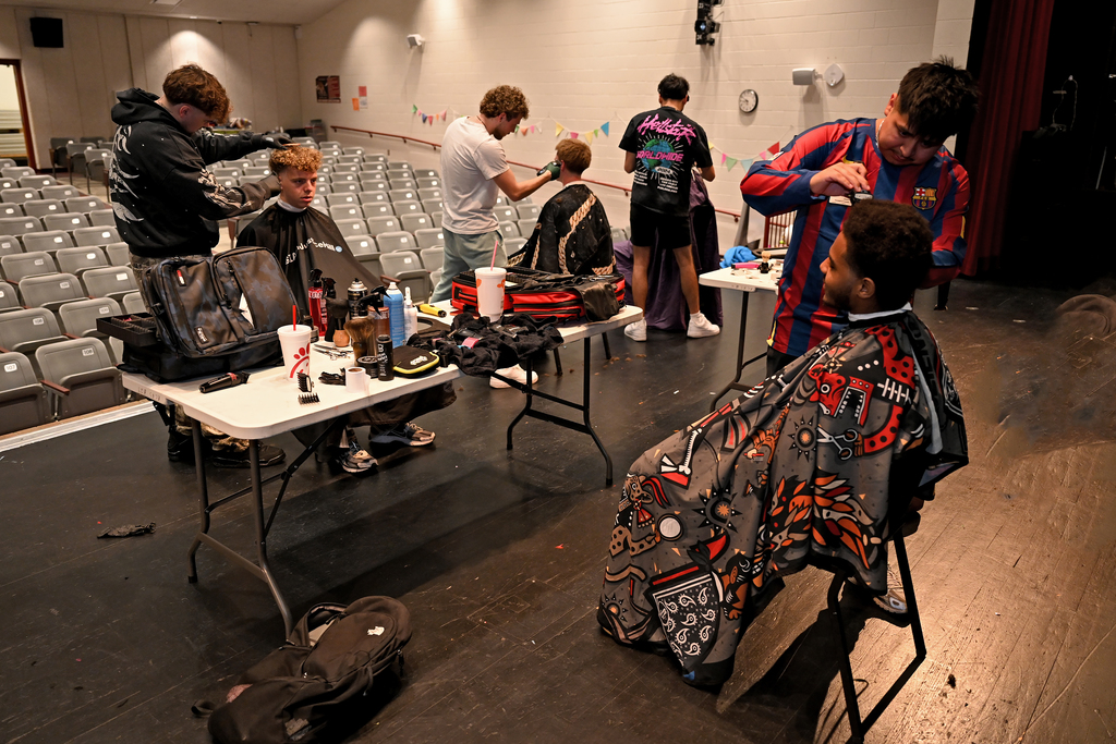 People in a large room with chairs and tables, several people getting a haircut.