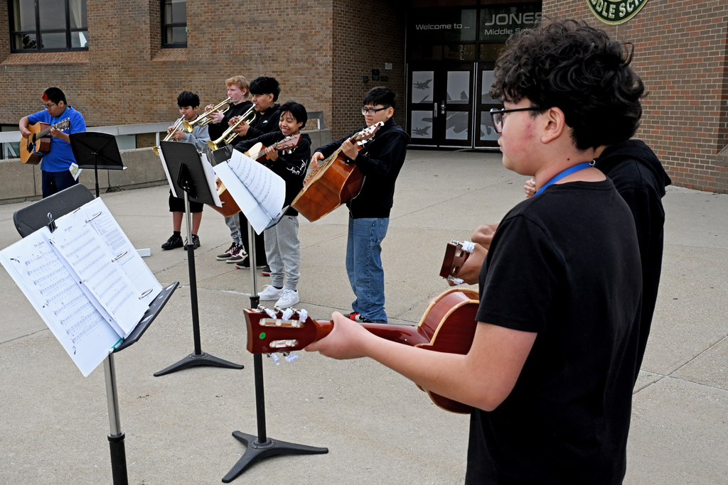 A group of students in a school yard, playing various musical instruments, with sheet music on stands.