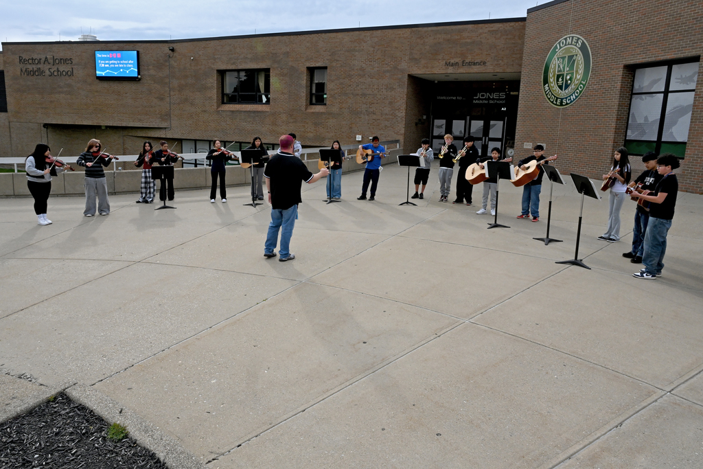 A group of individuals play musical instruments outside a building with a large window and sign.
