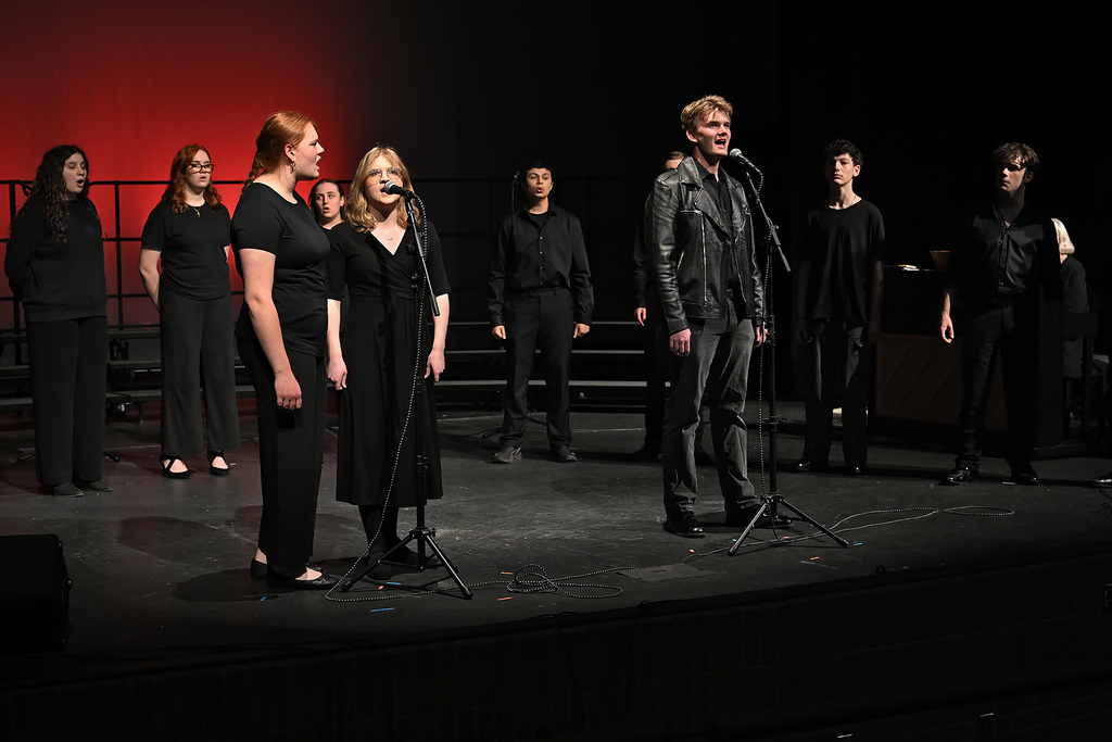 A group of people in dark clothing on a stage with microphones, one man with a leather jacket.