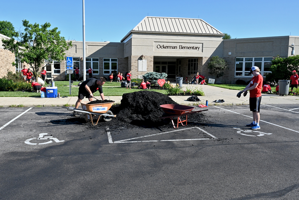 People in red shirts are using wheelbarrows to remove piles of mulch in front of a building.