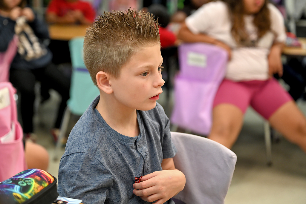 A boy with short, spiky hair wearing a blue shirt listens intently in a classroom.