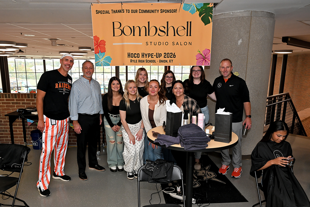 Group of people around a table with hair products. A banner with the words "Bombshell Studio Salon" above.