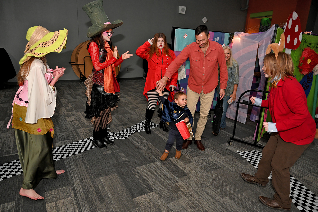 Group of adults and children dancing in a room with a checkered floor and colorful props.