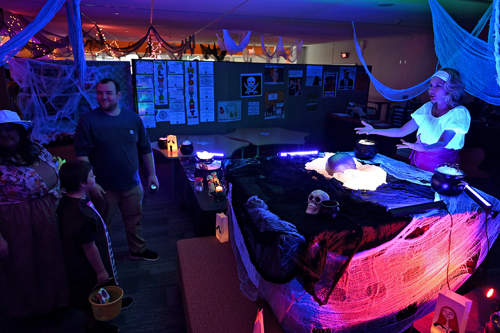 People inside a room with dim lighting and decorations. A woman speaks to a group near a table.