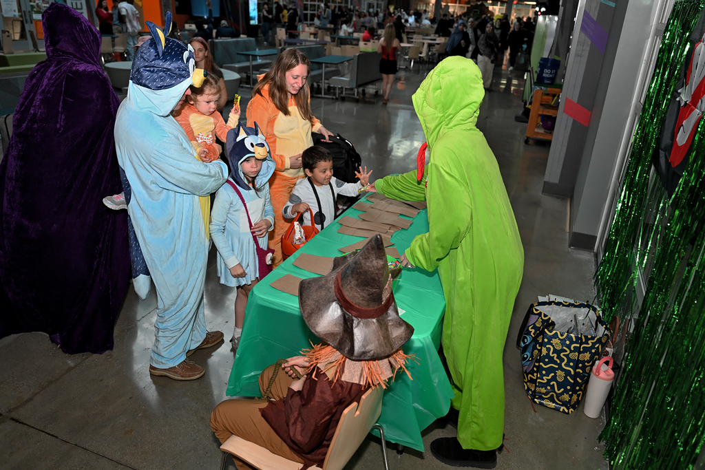 Several adults in costumes with children in costumes, standing by a table covered with green cloth.