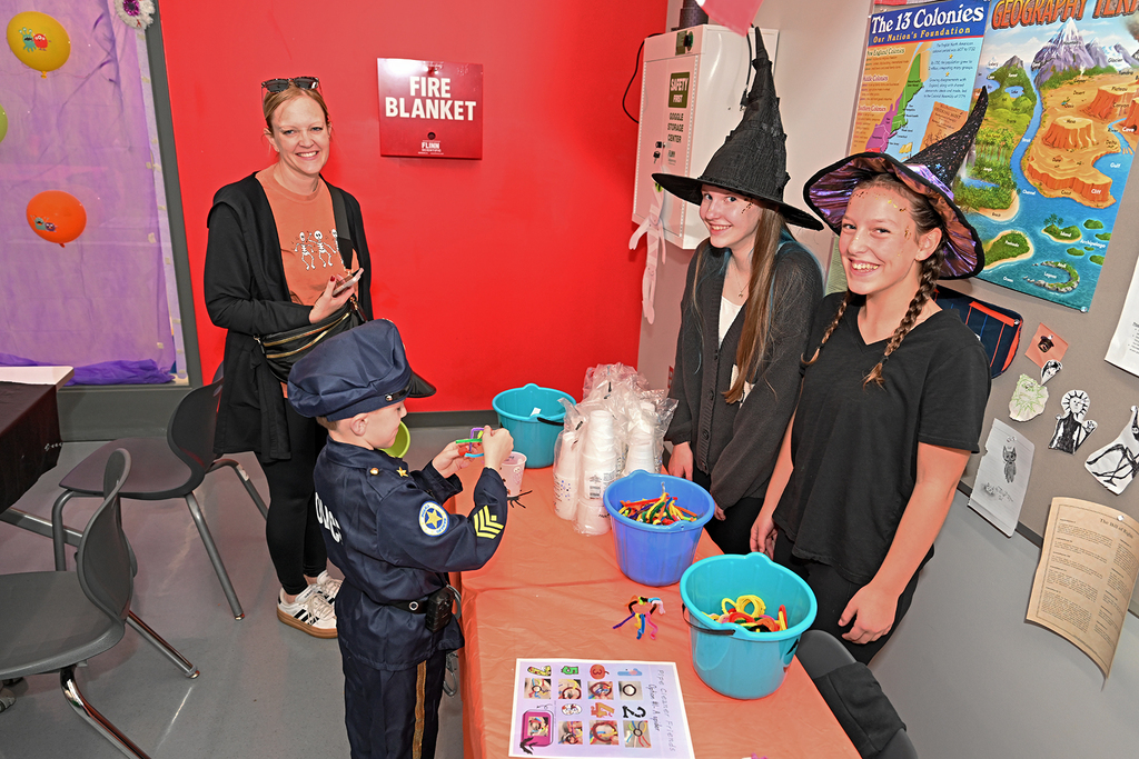 Four people at a table with buckets of candy. A girl in a police uniform is taking candy.