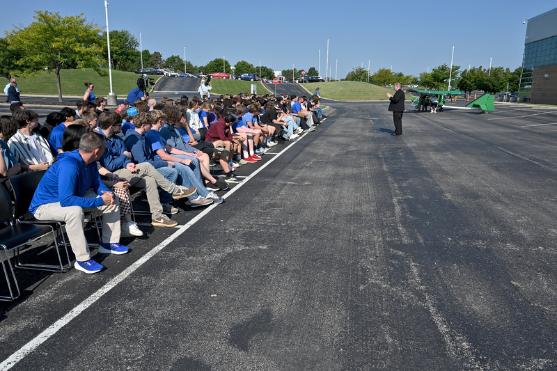 man speaking to student group in front of an airplane