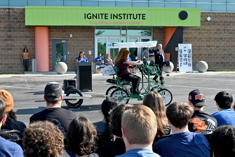 students riding four wheeled bike in front of other students