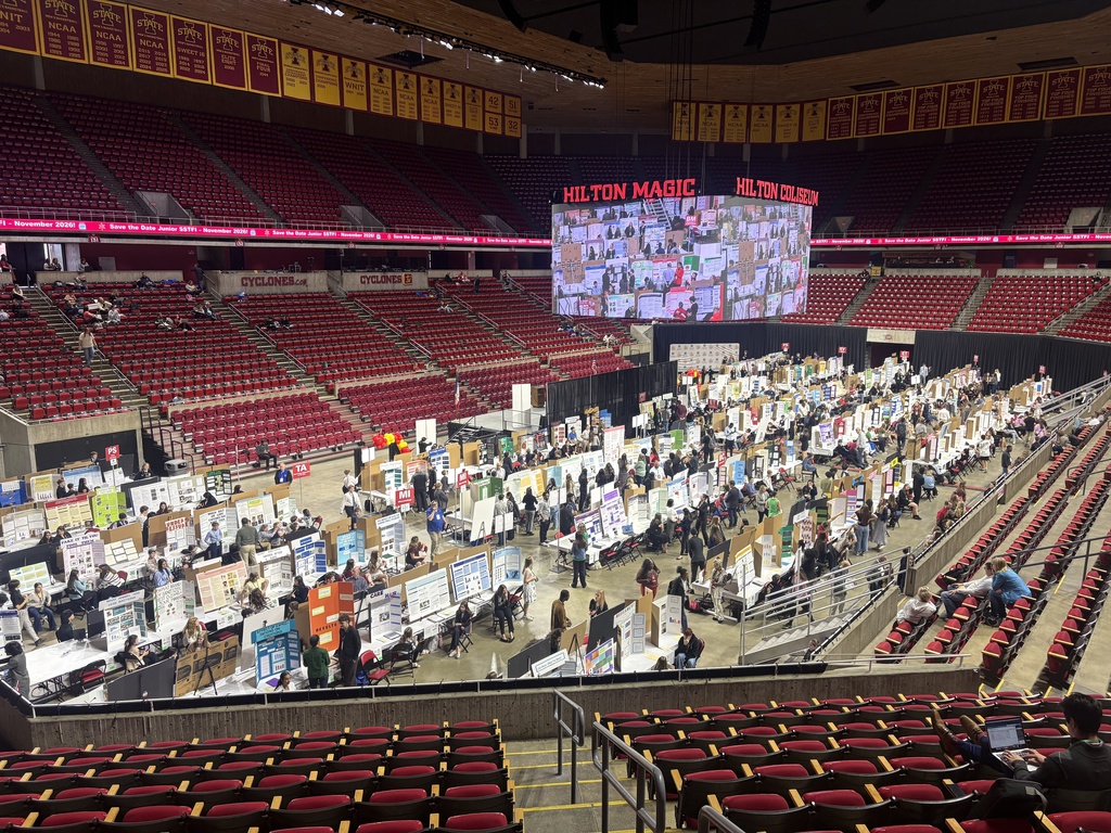 Large indoor arena filled with rows of science fair project boards and participants presenting to judges.
