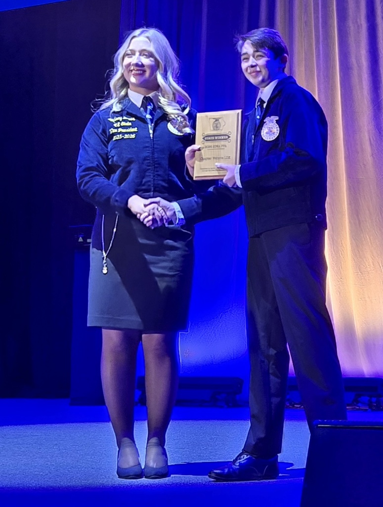 Isaac Sorensen on stage shaking another person's hand while receiving a plaque.