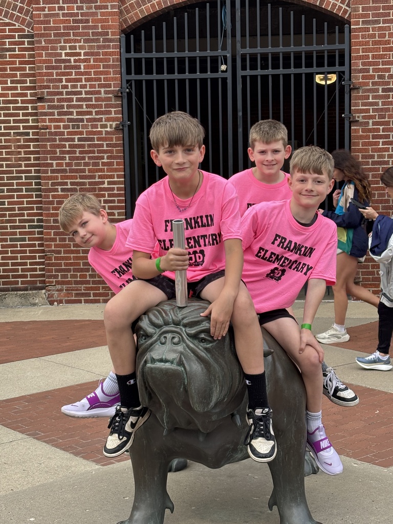 Four young students sitting on the Drake Bulldog sculpture in front of the stadium entrance.