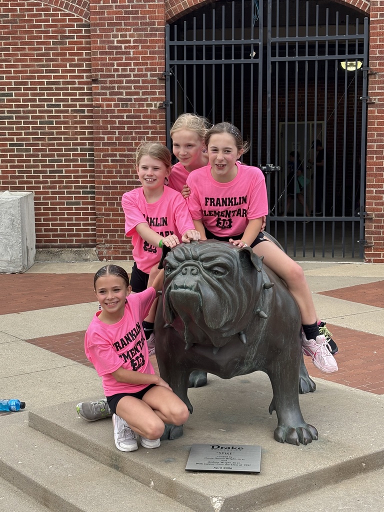Four young students sitting on the Drake Bulldog sculpture in front of the stadium entrance.