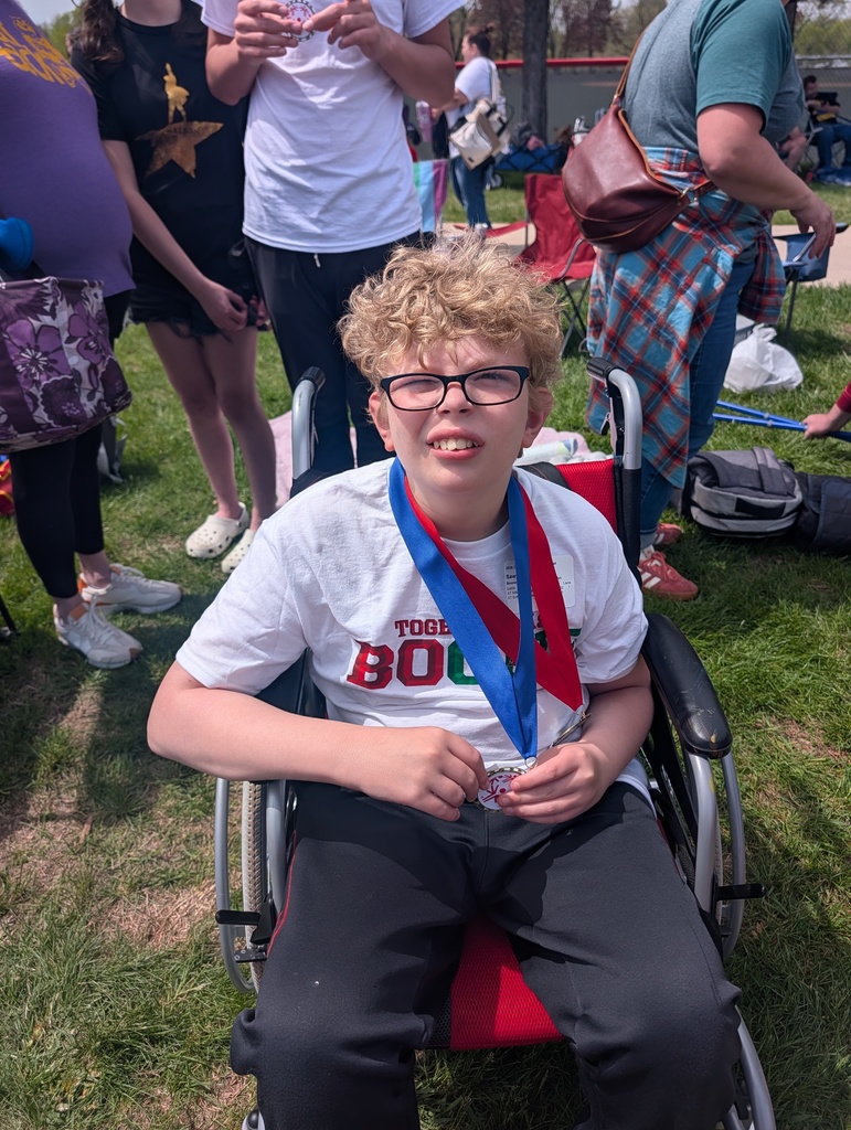 Student in a white shirt that says Boone, sitting in a wheel chair and wearing medals around neck.