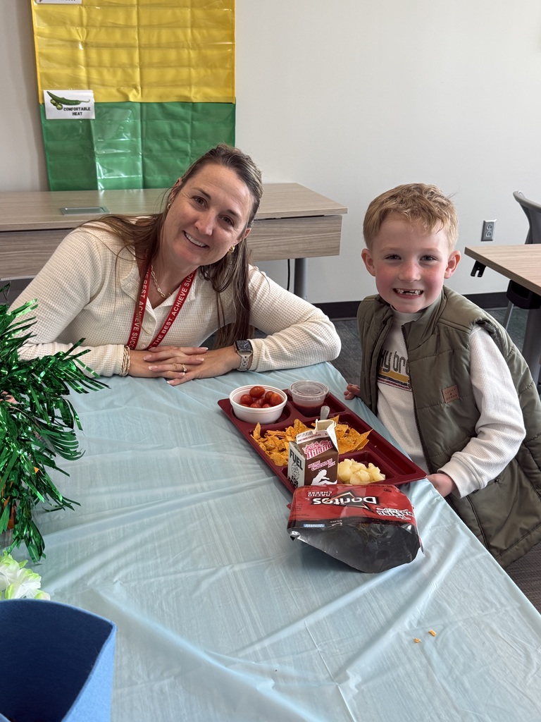 Student sitting at a table with a lunch tray, next to an adult.