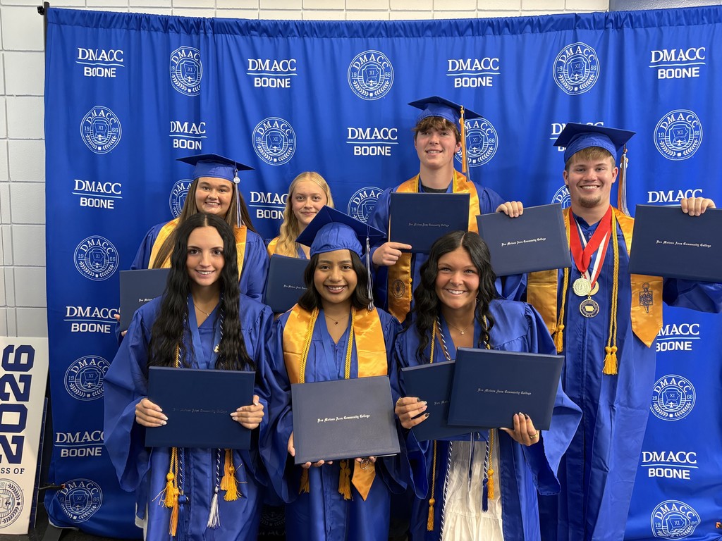 Seven high school students in blue gowns and caps holding navy blue diplomas that say "Des Moines Area Community College."