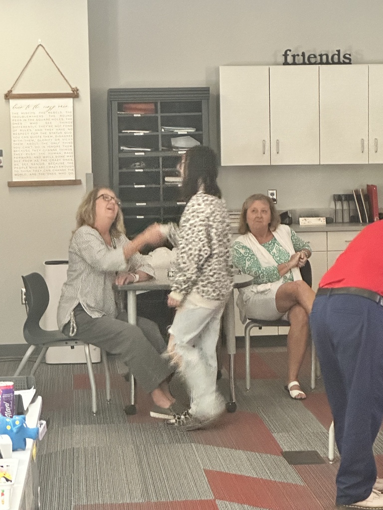 Two women seated at a classroom table talk with a standing student.