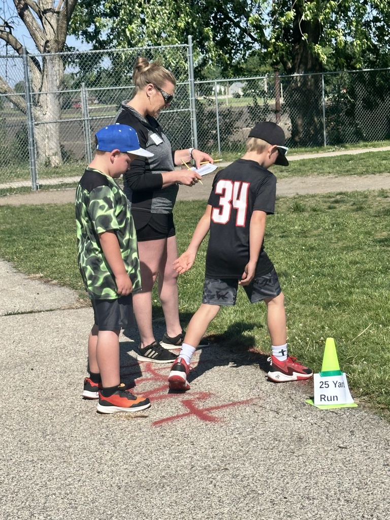 Students line up for a 25-yard run while a staff member records results beside a school sidewalk.