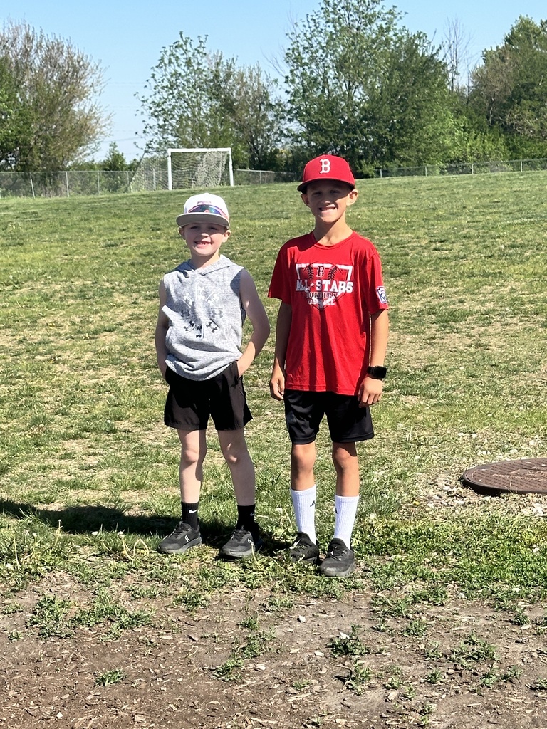 Two young boys smile and pose together on a grassy school field during an outdoor activity day.