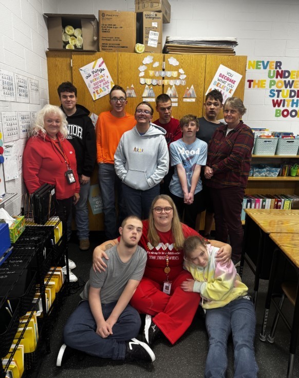 Mrs. Allen seated on the floor with students and paras from her classroom