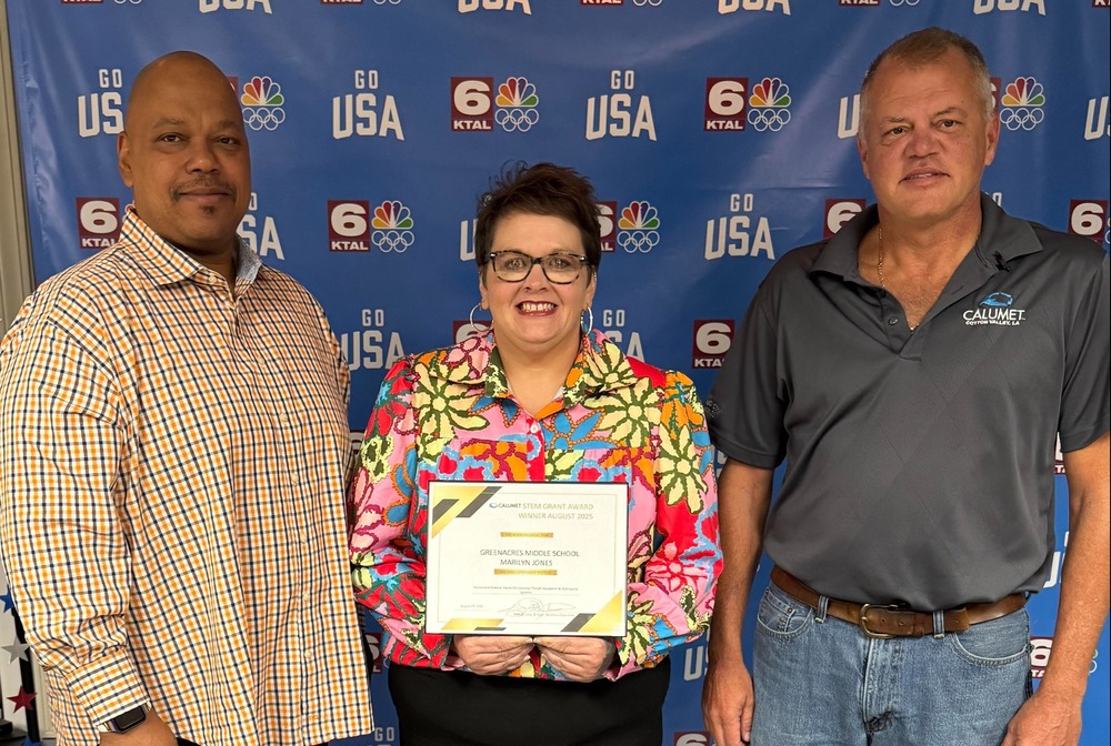Photo of teacher Marilyn Jones holding a certificate, flanked by Calumet representatives