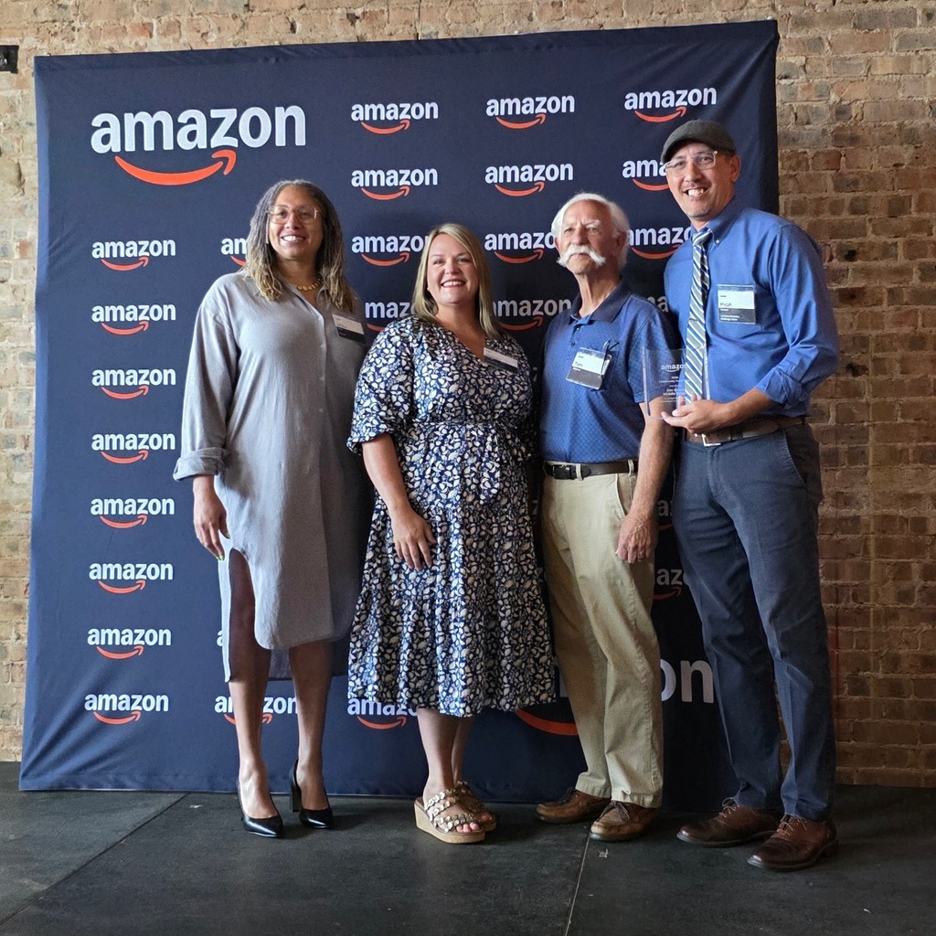 Elm Grove Middle teacher Micah Stewart along with three representatives  posing in front of an Amazon banner. 