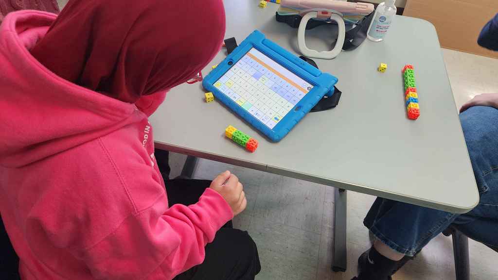 A student using her AAC to help play games with friends.