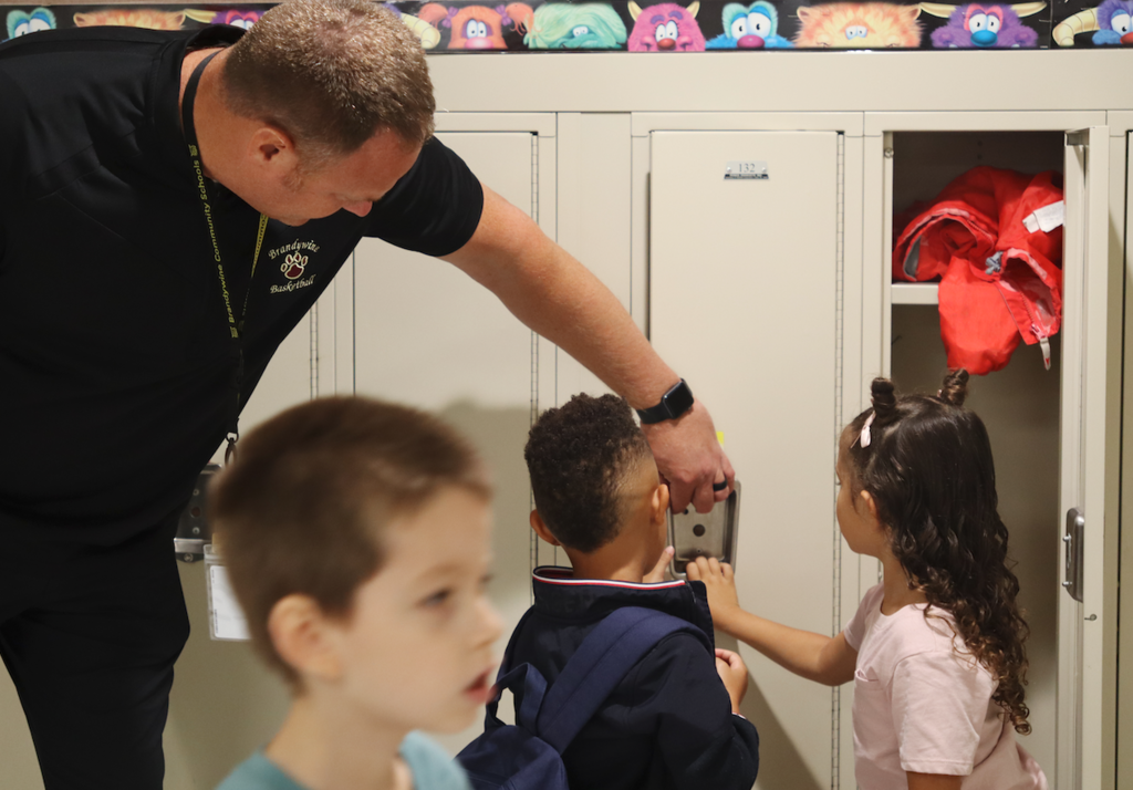 adult man helping two kids open a locker