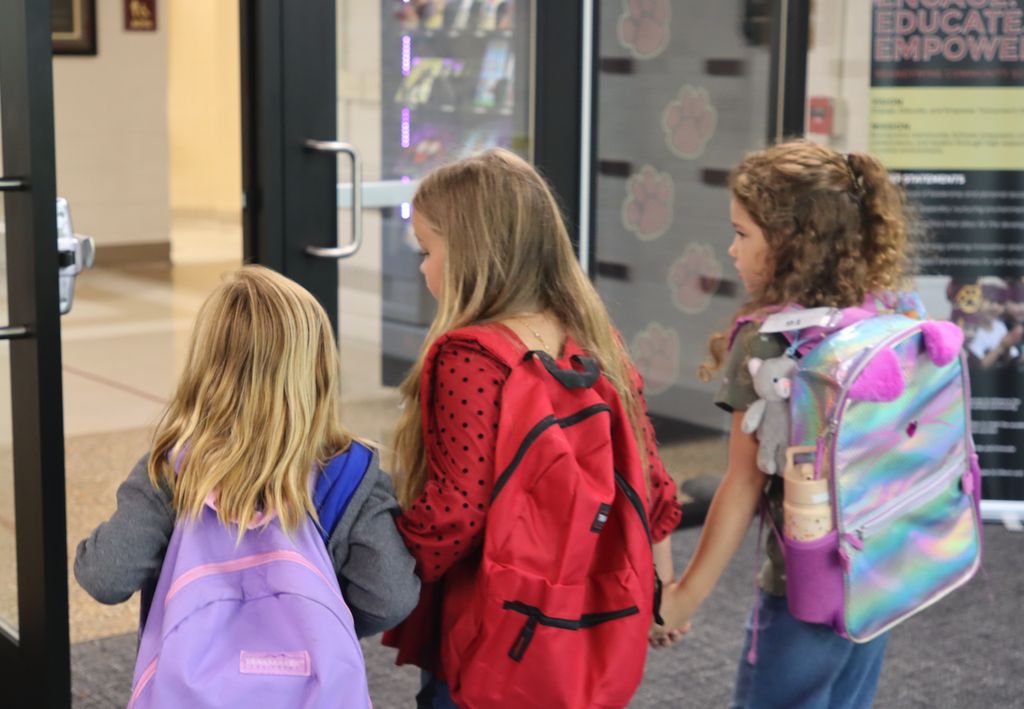 three little girls walking into school with backpacks holding hands