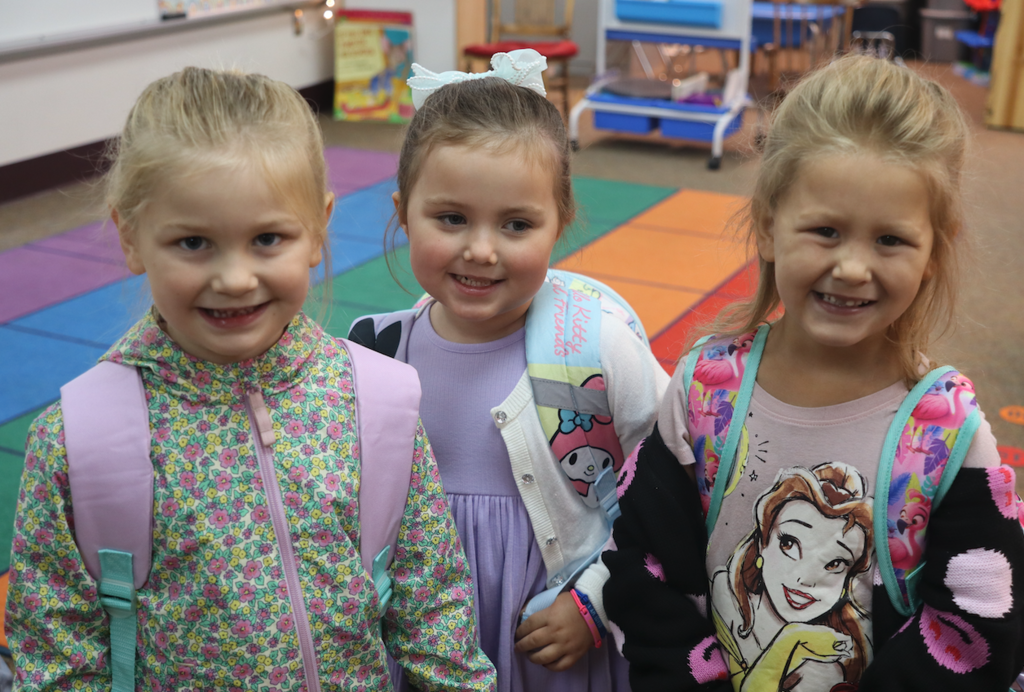 three little girls wearing their backpacks in a classroom