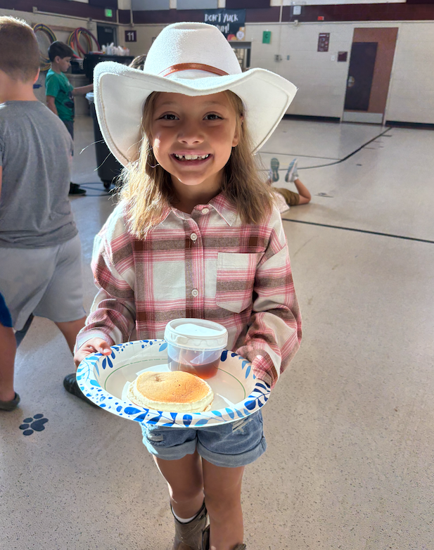 little girl wearing cowboy hat holding plate with pancakes 