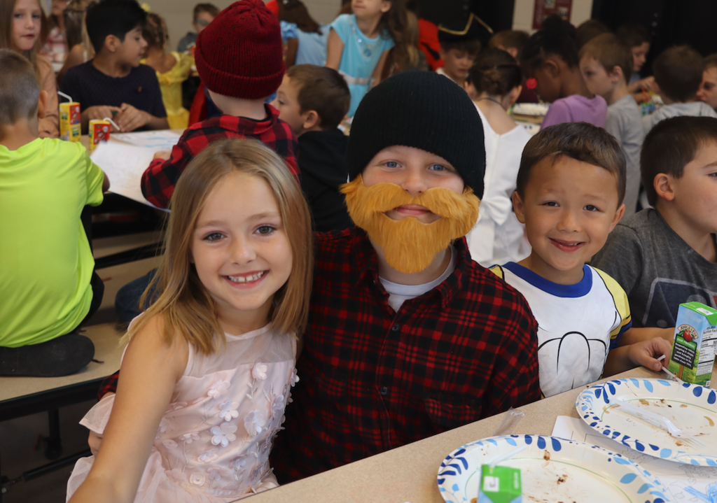 three little kids, two boys and one girl sitting at the cafeteria table