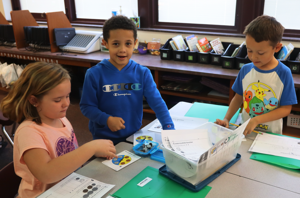 three little kids playing at a table with fake coins