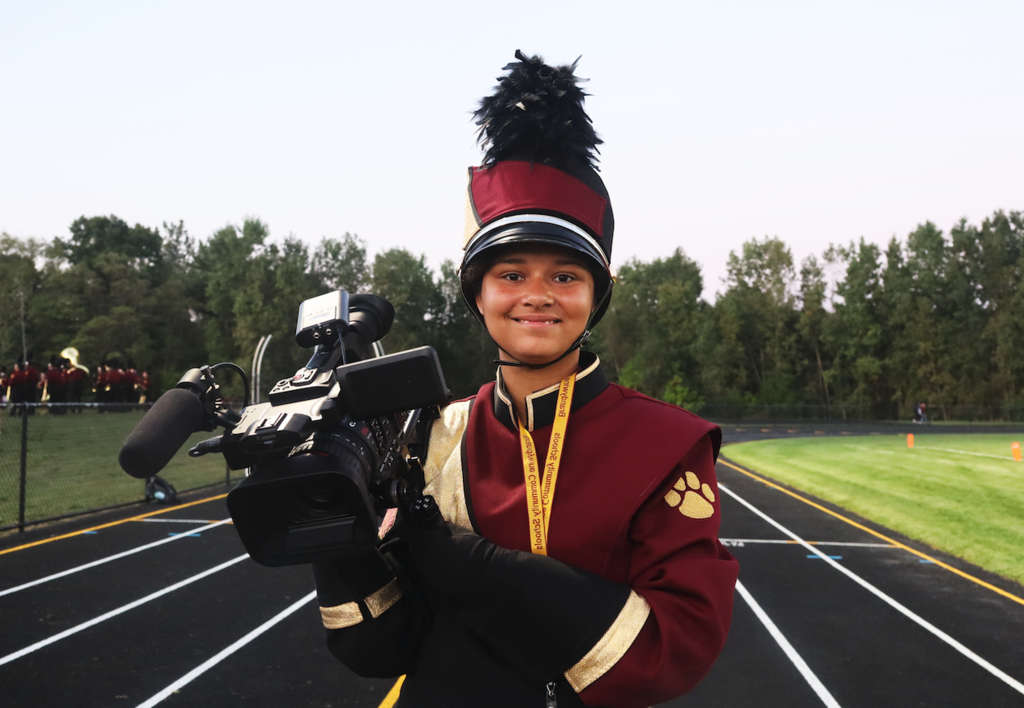student in marching outfit and camera