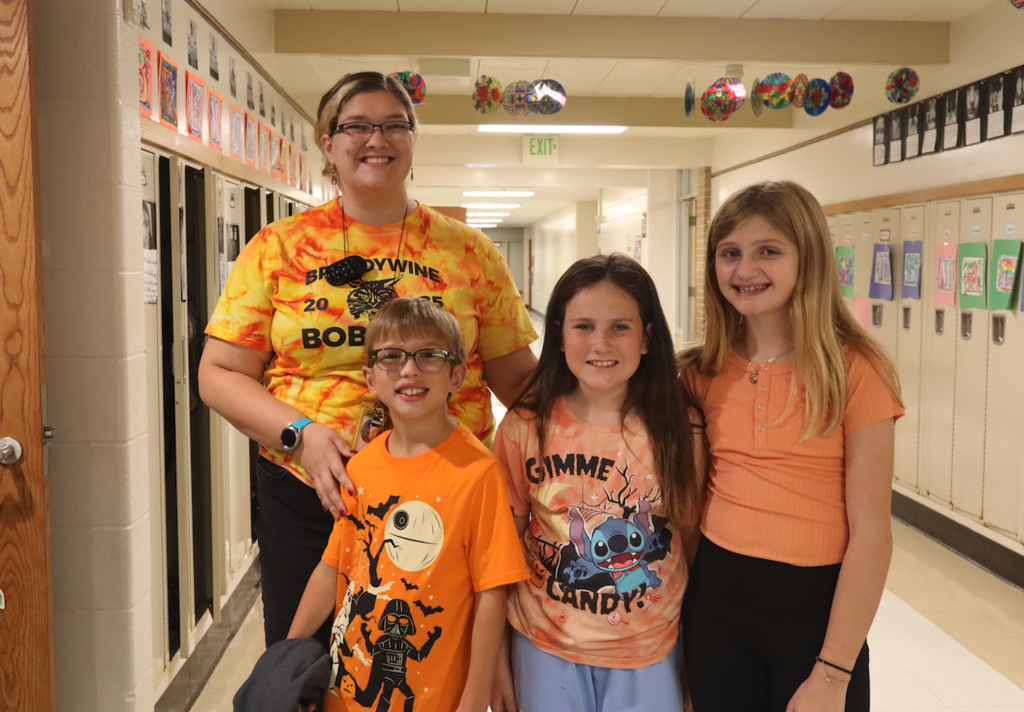 3 students and teacher in orange shirts