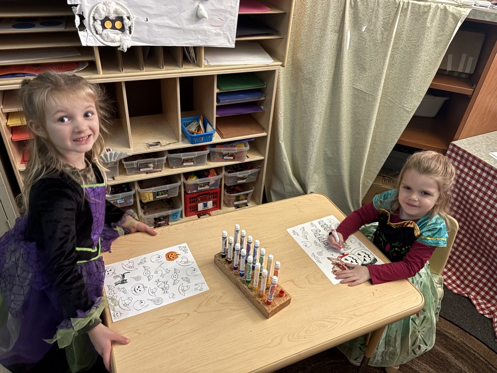 two little girls coloring at table in princess costumes