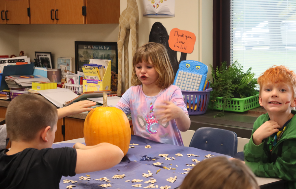 girl reaching for pumpkin with other students at table with her