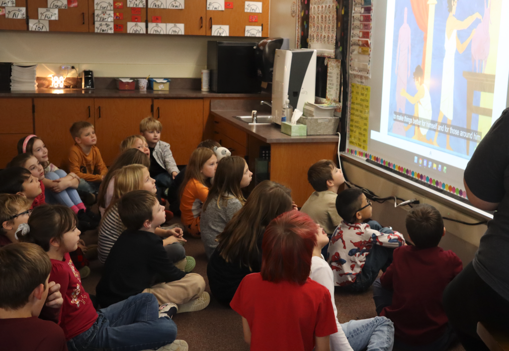 students sitting on the floor watching a video in class