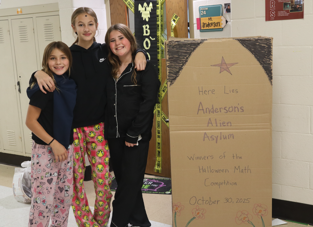 three students in front of a cardboard "tombstone"