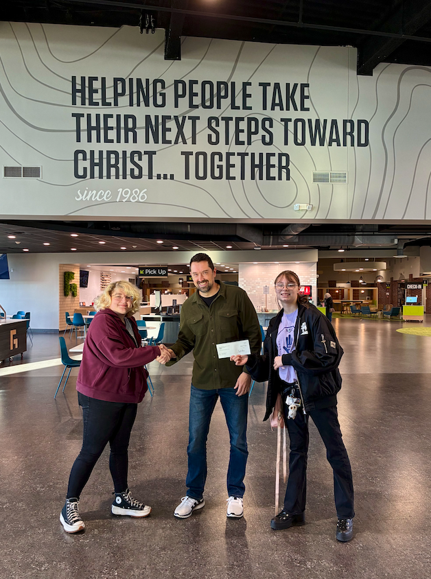 two students handing pastor a check and shaking his hand