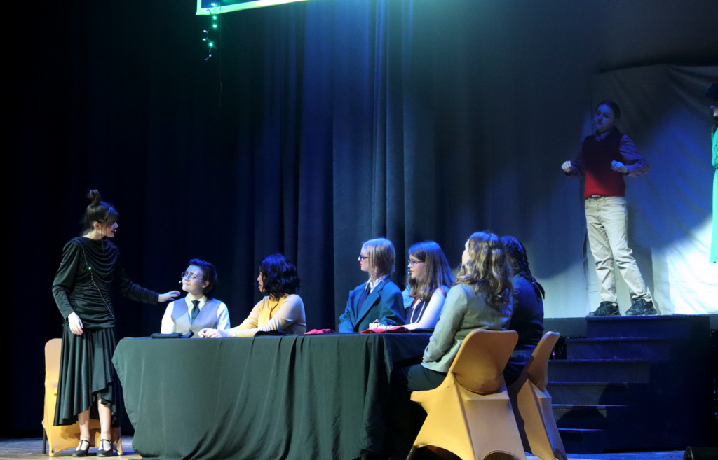 group of students sitting at a table on stage