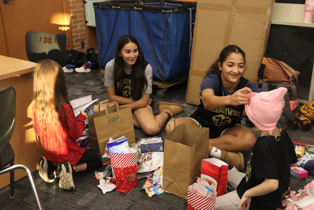 2 teenage girls with 2 smaller girls opening presents and putting hats on head