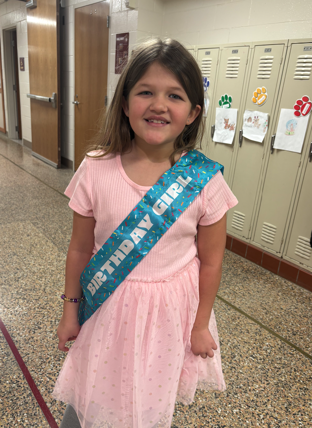 little girl wearing a pink dress and a birthday sash 