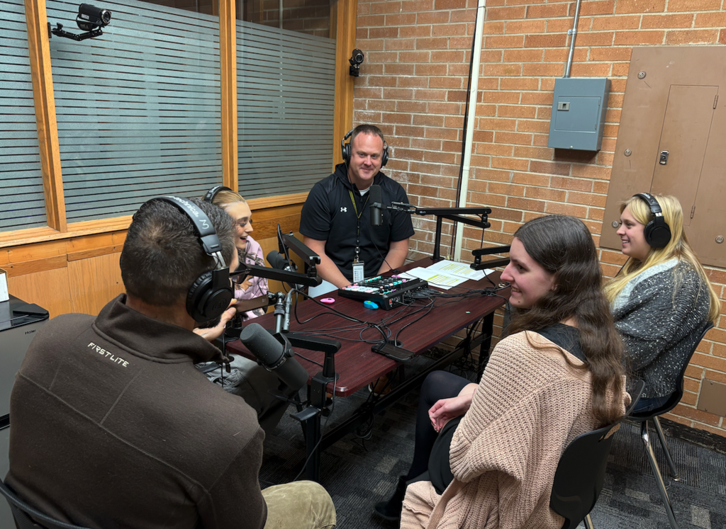 students sitting with mr. walker at microphone podcast table