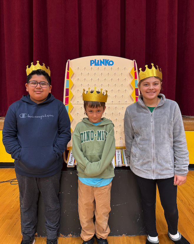 three students wearing crowns in front of a plinko game
