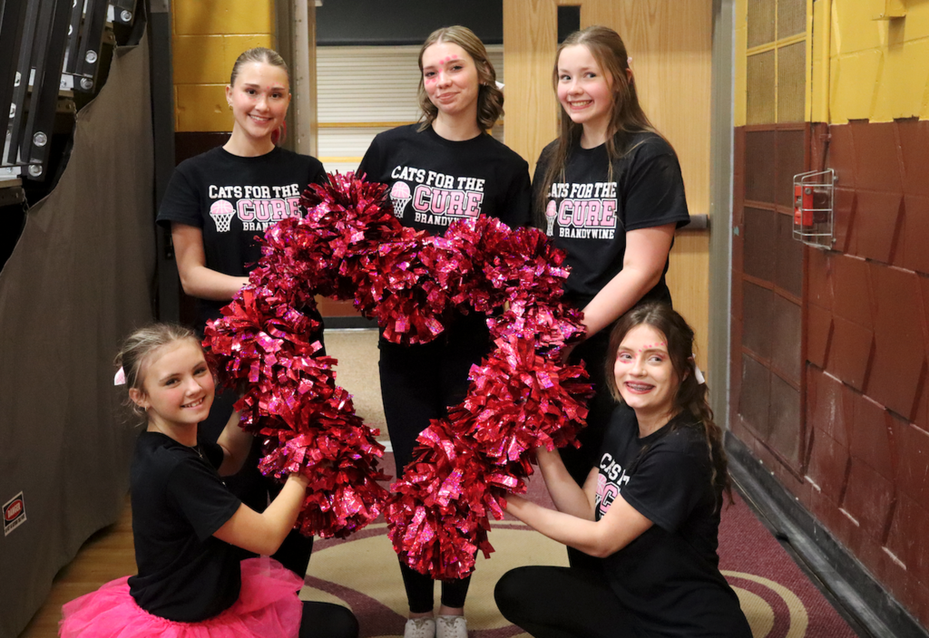 cheerleaders making a heart shape with pink poms poms
